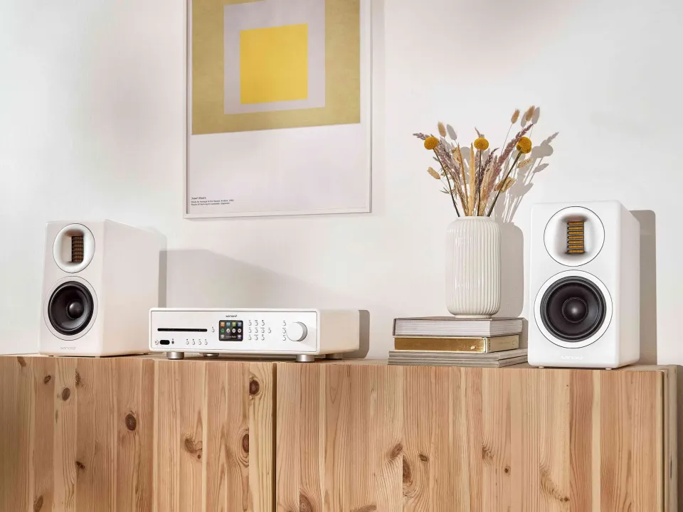 Weiße Regallautsprecher mit Audiogerät auf einem Holz-Sideboard