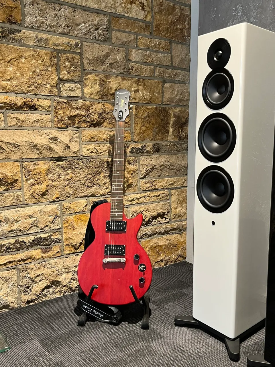 Rote E-Gitarre neben einem weißen Standlautsprecher vor einer Natursteinwand