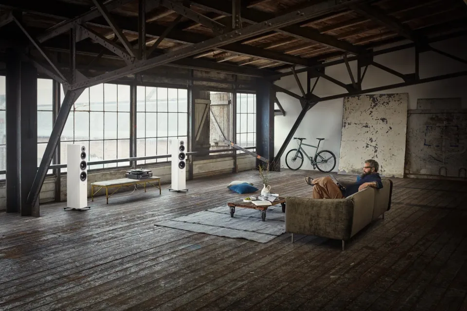 Industrieloft mit weißen Standlautsprechern, ein Mann sitzt auf dem Sofa