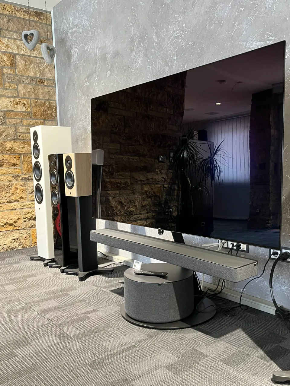 Großer Fernseher mit Soundbar und Standlautsprechern vor einer Natursteinwand