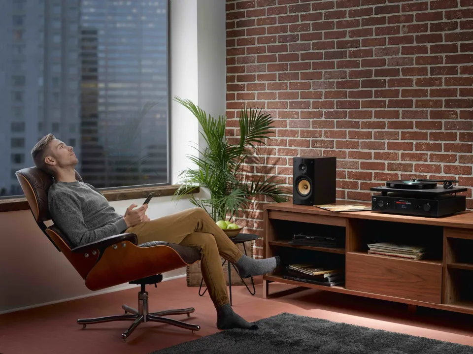 Mann im Lounge-Sessel hört Musik, im Hintergrund Lautsprecher und Plattenspieler