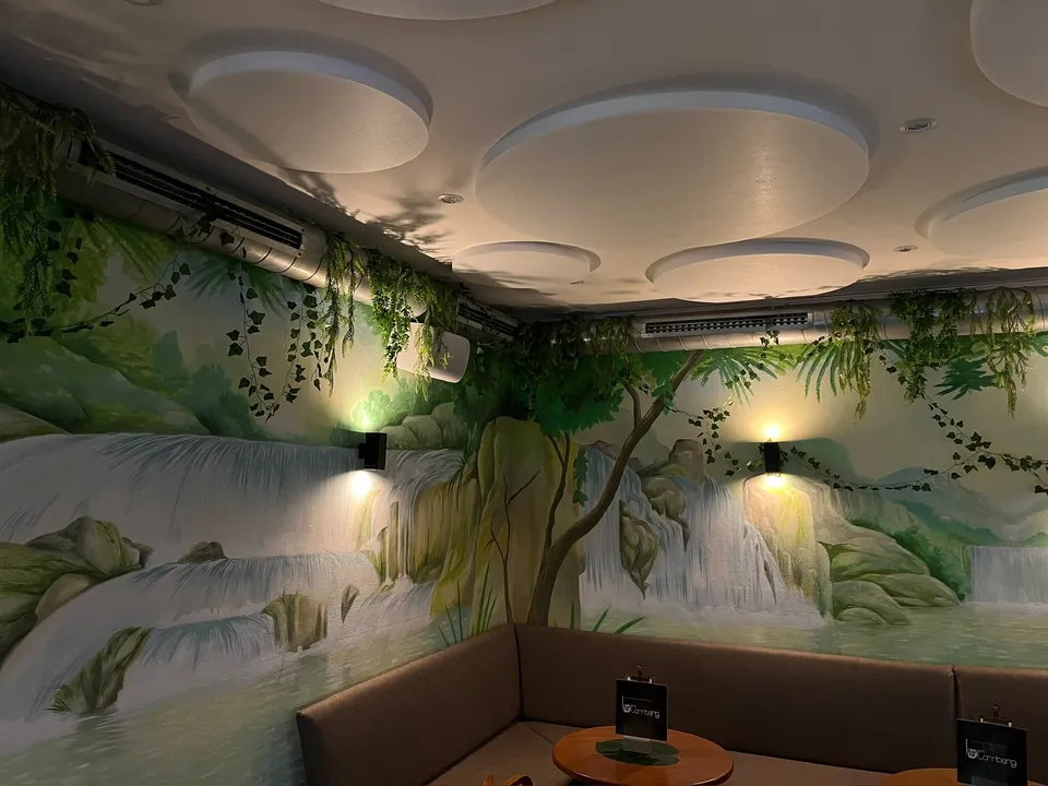 Sitzecke unter der Akustikdecke vor einem Wandbild mit Wasserfall