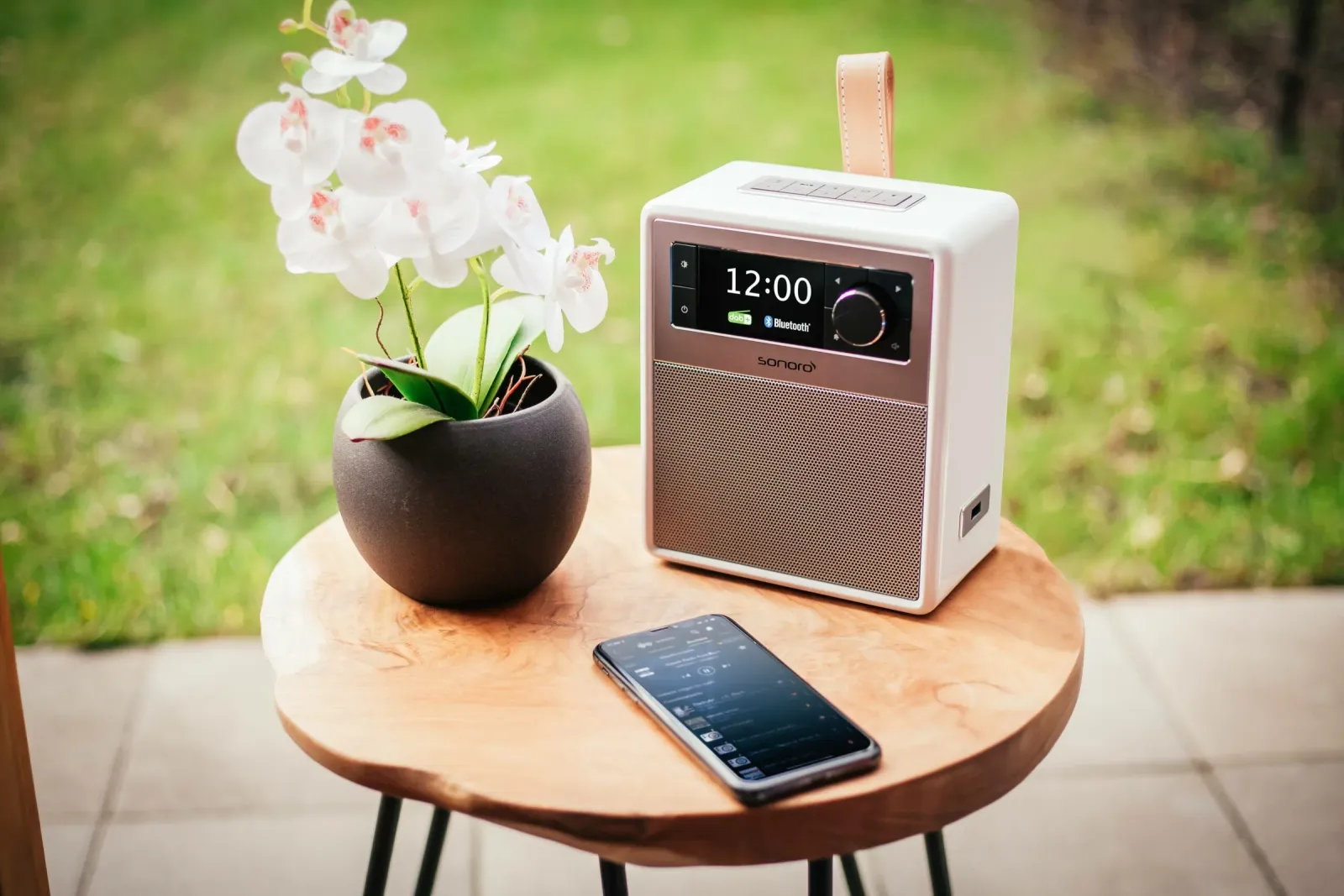 sonoro-Radio mit Ledergriff und Smartphone auf einem Gartentisch