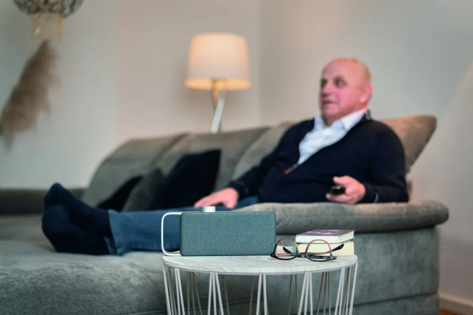 Älterer Mann auf dem Sofa, der faller-Lautsprecher steht auf dem Beistelltisch