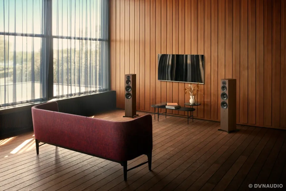 Wohnraum mit Holzwand, Wandfernseher, zwei Standlautsprechern und rotem Sofa