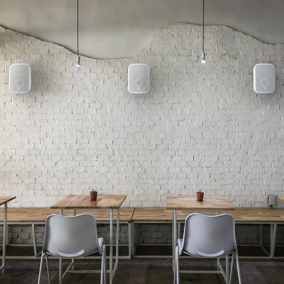 Café mit drei weißen Wandlautsprechern an einer Backsteinwand