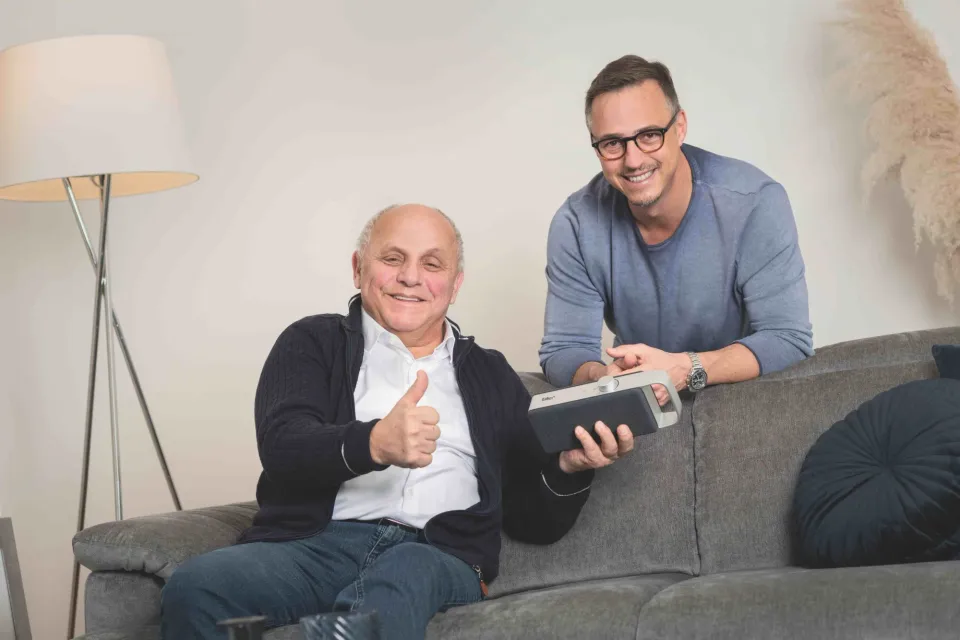 Zwei Männer auf dem Sofa mit dem faller-Lautsprecher, einer zeigt den Daumen nach oben