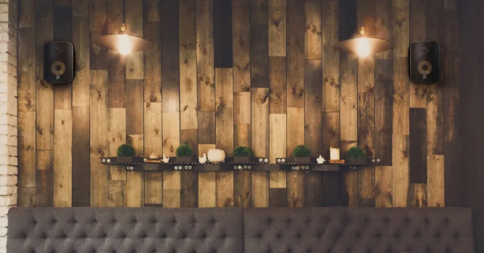 Holzwand mit zwei schwarzen Wandlautsprechern über einer Sitzbank